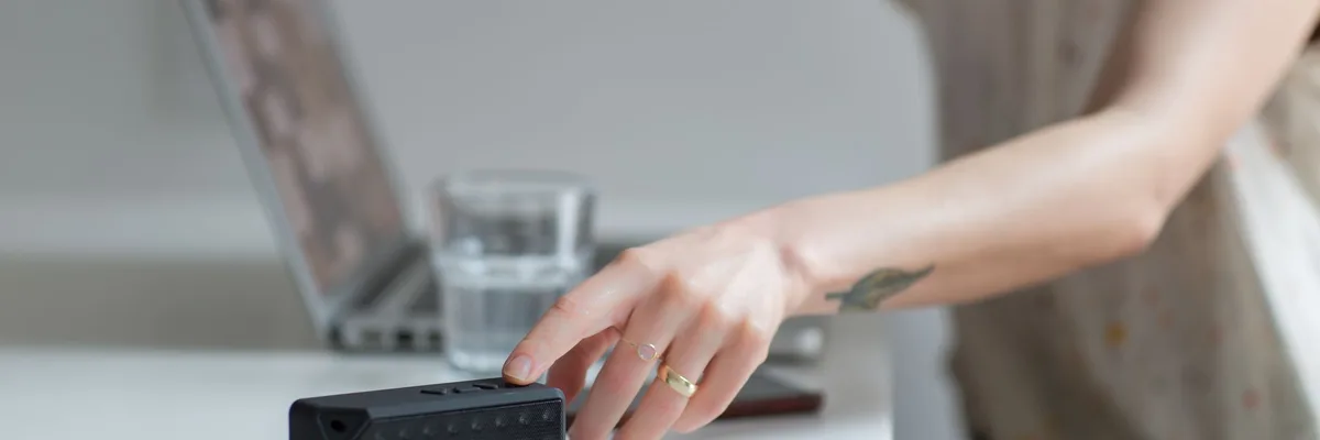 Gros plan sur une main atteignant un haut-parleur sans fil sur un bureau à côté d'un ordinateur portable.